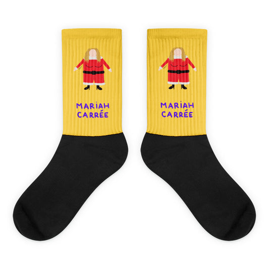 Paire de chaussettes jaunes et noires illustrant un personnage féminin carré en costume de Noël rouge, avec l'inscription "MARIAH CARRÉE" en lettres violettes.