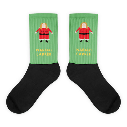 Paire de chaussettes vertes et noires illustrant un personnage féminin carré en costume de Noël rouge, avec l'inscription "MARIAH CARRÉE" en lettres jaunes.